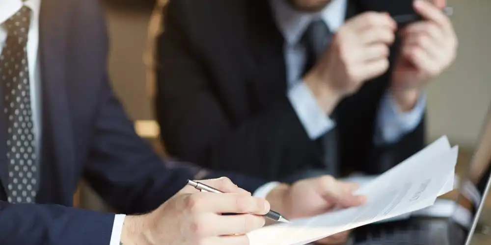 Closeup portrait of two unrecognizable  business partners reviewing paperwork and signing contract papers at table during meeting